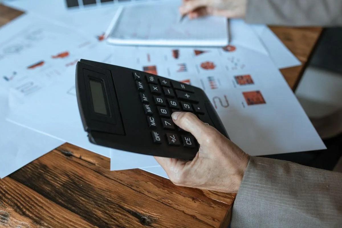 Pessoa usando uma calculadora sobre relatórios econômicos e dados estatísticos para entender como o PIB é calculado.