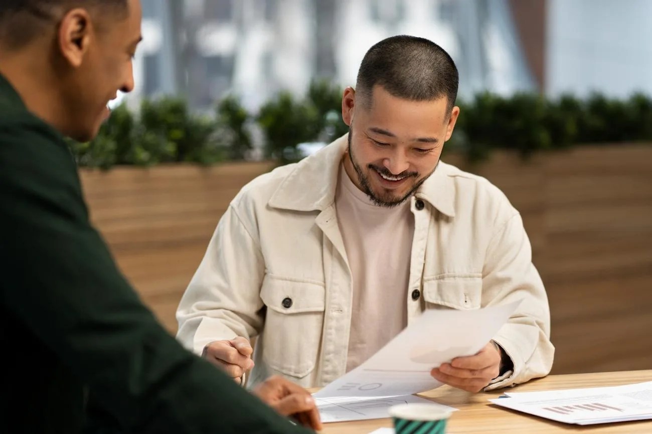 Dois profissionais reunidos em um ambiente corporativo, estudando o mercado financeiro, analisando gráficos e trocando conhecimentos para tirar certificações da Anbima.