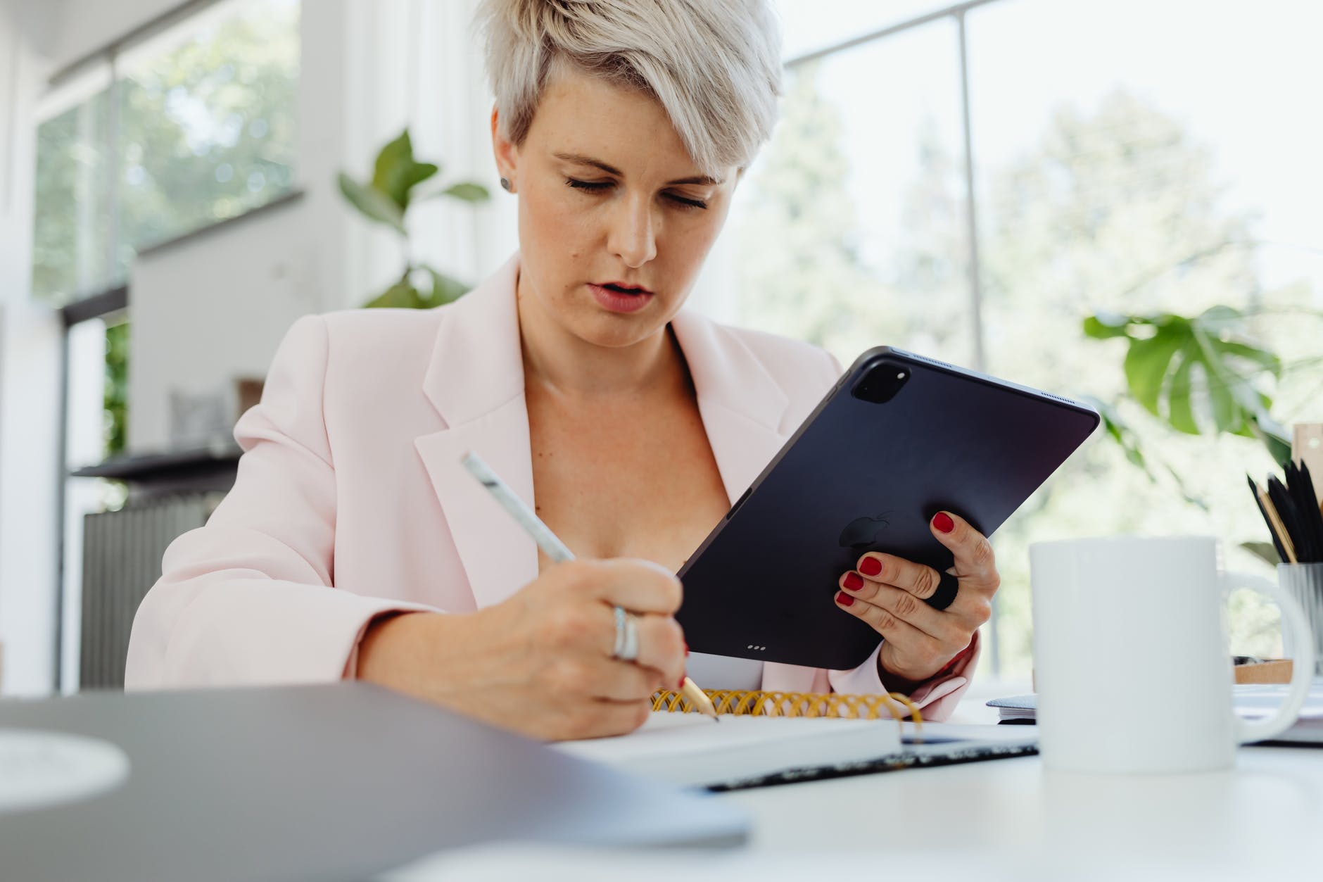 Mulher com tablet na mão e um caderno sob a mesa. Ela está anotando algo sobre liquidez.