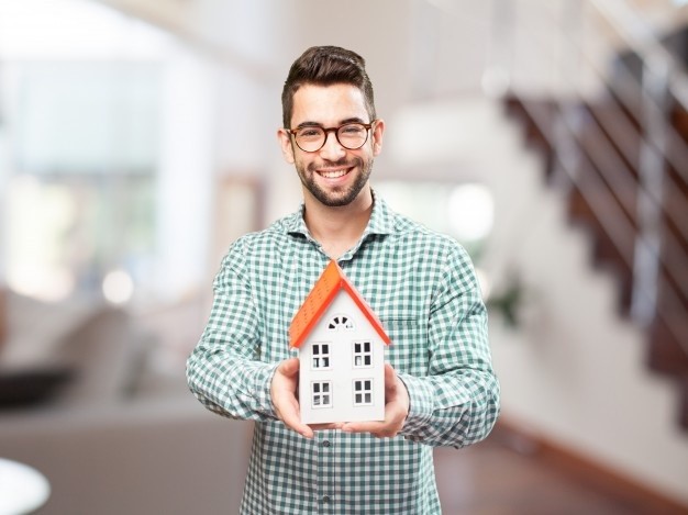 Homem segurando uma mini casa e sorrindo após entender o que é INCC e como isso impacta sua compra