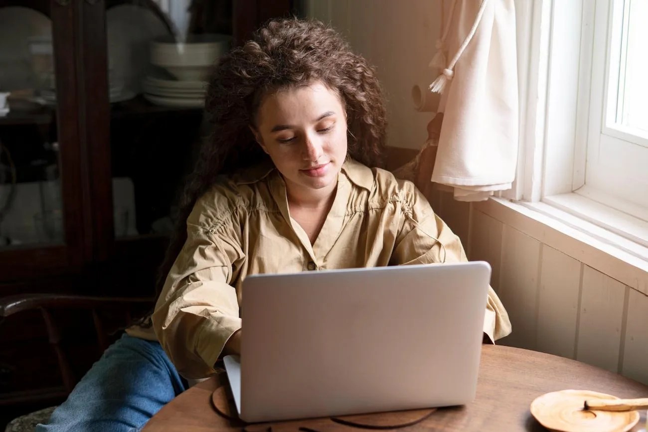 Mulher usando notebook perto da janela, pesquisando se vale a pena investir no mercado de opções.