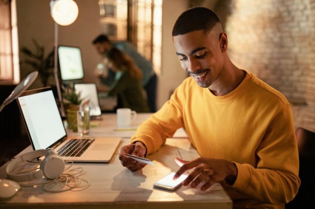 Jovem rapaz consulta seu saldo investback em seu celular enquanto segura o cartão XP em outra mão.