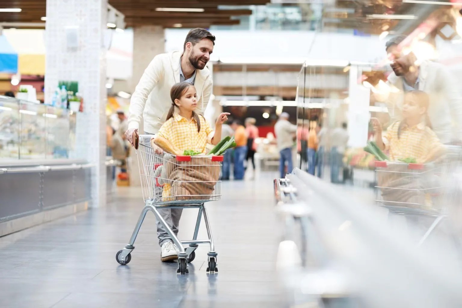 Homem empurrando carrinho de supermercado com uma criança sentada entre as compras, ilustrando o poder de compra das famílias em um cenário de estagflação no Brasil.