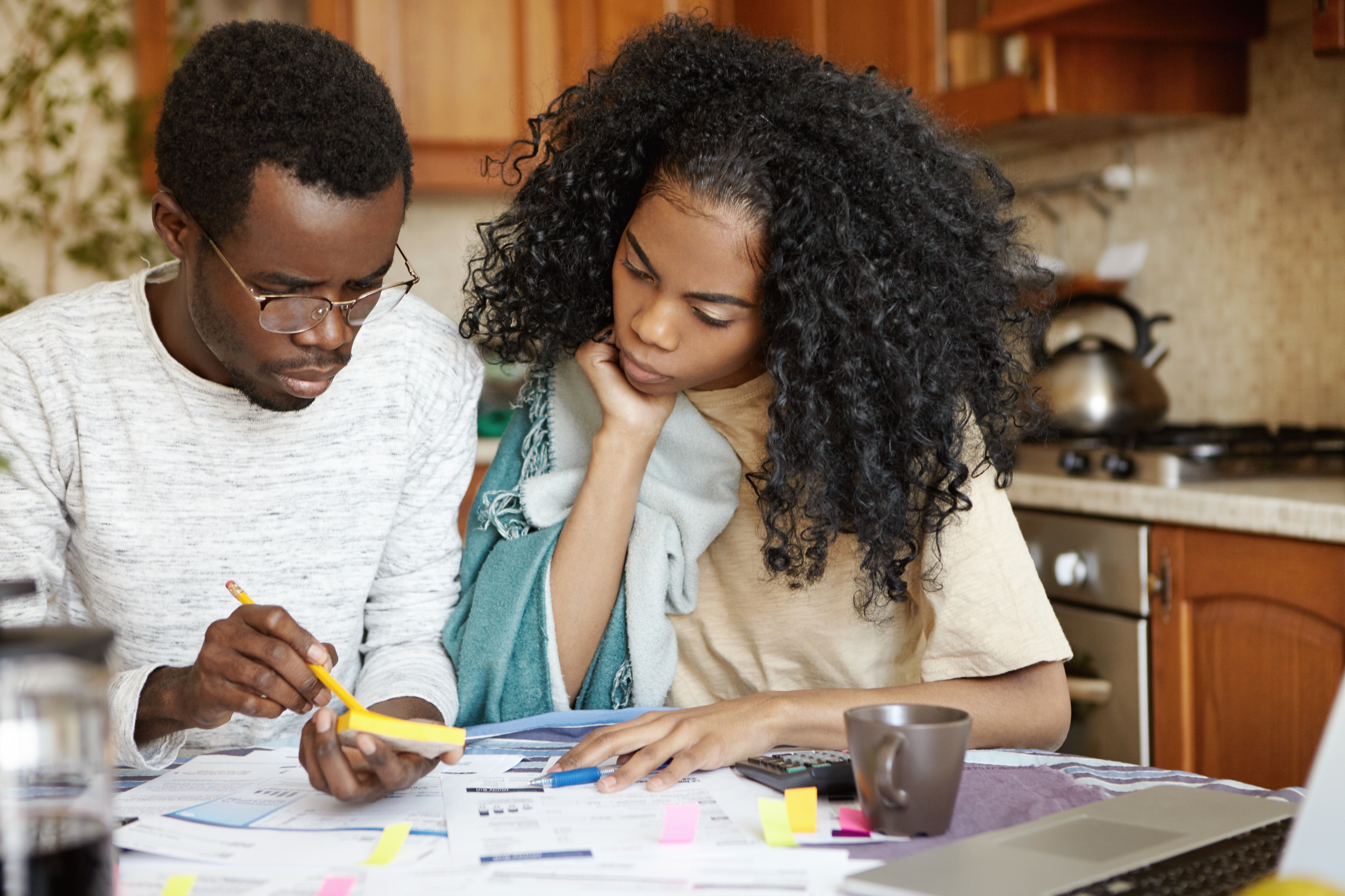 Casal com páginas, post-it, calculadora e canetas na mesa. Eles estão estudando possibilidades de investimentos, inclusive os derivativos.