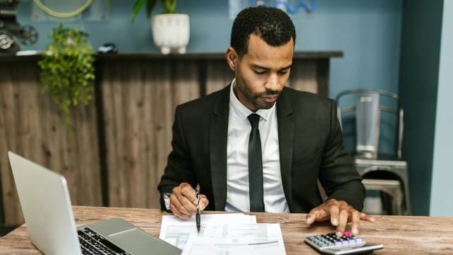 Homem investidor comparando valores em um papel e fazendo cálculos em uma calculadora.