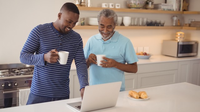 Fotografia de pai e filho adultos tomando café e discutindo de forma tranquila sobre o planejamento sucessório em um notebook.