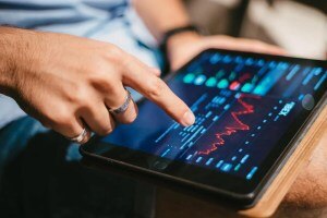 Pessoa usando tablet com gráficos financeiros e linhas de tendência, analisando dados de mercado para avaliar se vale a pena investir em ETF.